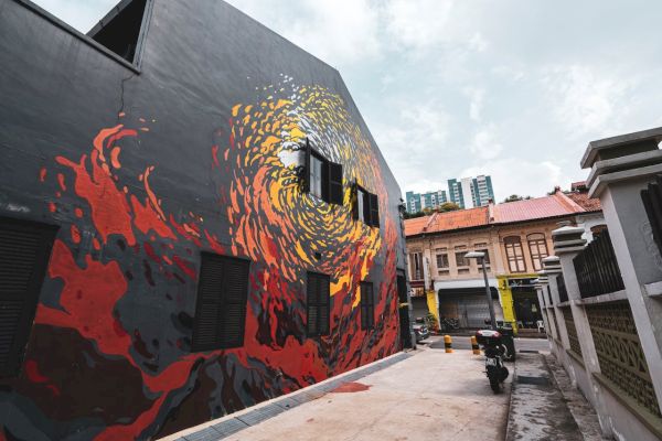 A vibrant street art mural on a building wall, depicting swirling colors, along a narrow alley with buildings, a motorcycle, and city in the background.