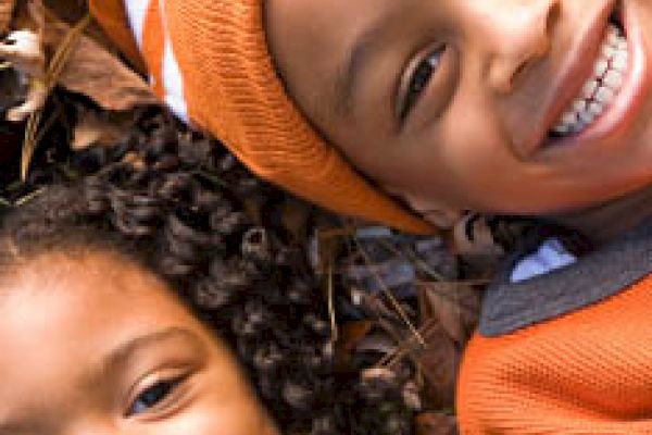 Two children lying on leaves, smiling happily, and wearing autumn-colored clothing.